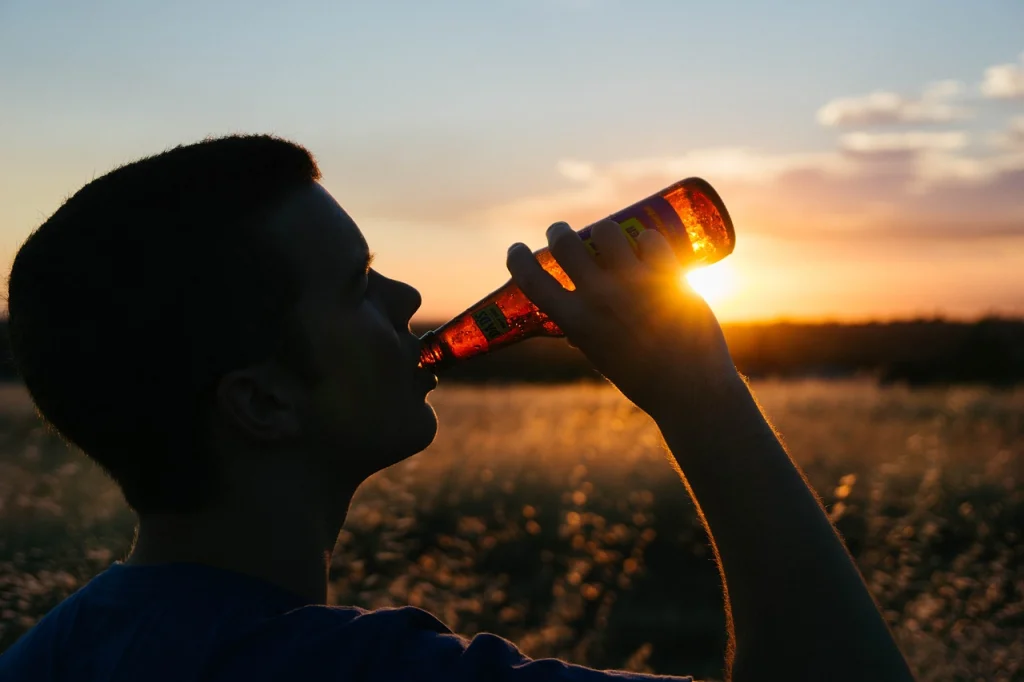 This image shows a man drinking from a bottle of beer in the middle of a field.