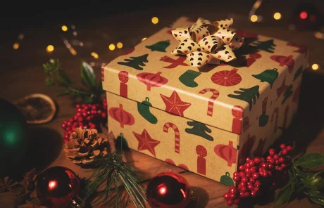 This image shows a gift box with Christmas prints surrounded by garland, mistletoe, string lights, and Christmas ornaments.